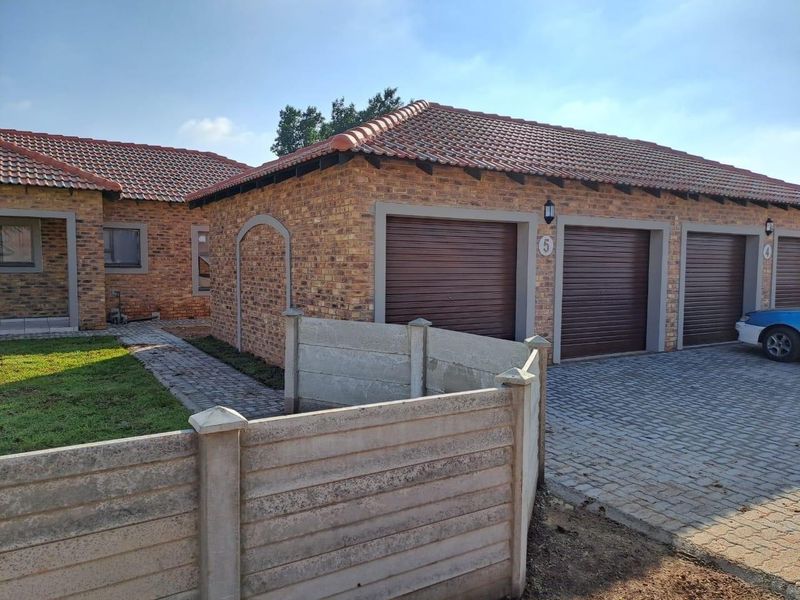 Front exterior view of a face brick townhouse featuring a triple garage with roll-up doors, paved driveway, and precast concrete boundary walling.