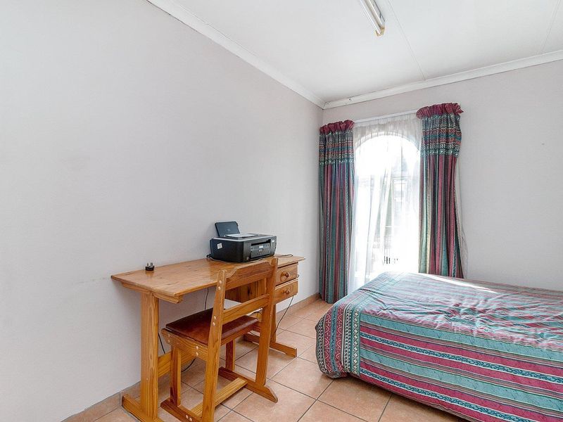 A functional bedroom featuring tiled flooring, a distinctive arched window, and coved ceiling detailing.