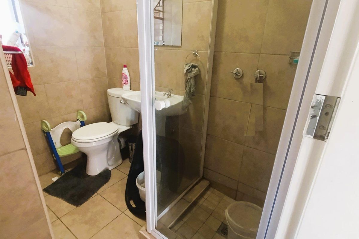 A functional bathroom featuring floor-to-ceiling wall tiles, a glass-enclosed shower, a pedestal basin, and a standard toilet.