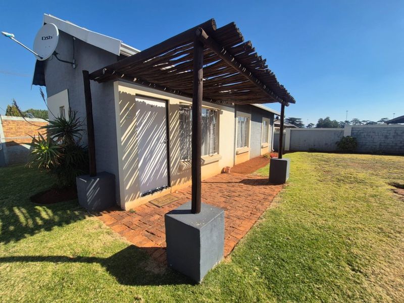 A paved outdoor patio area featuring a timber pergola structure, set within a private garden space with a boundary wall.