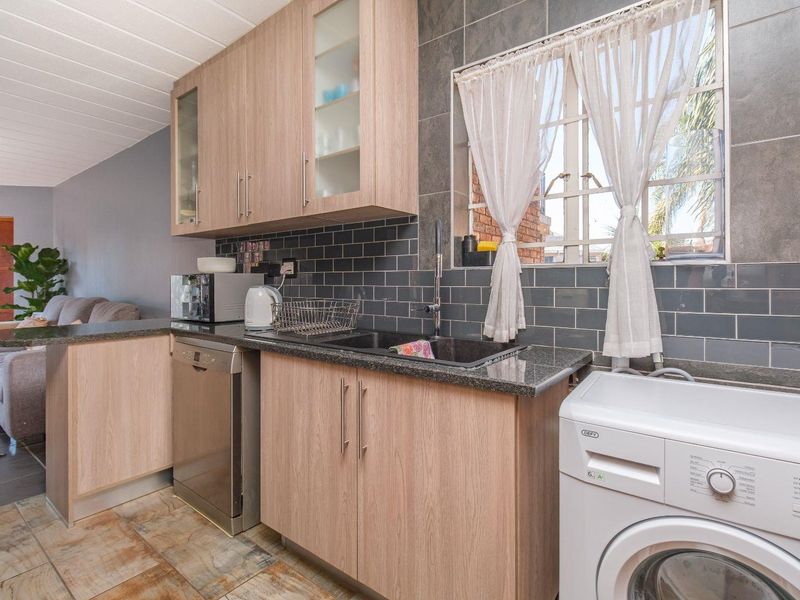 A functional kitchen featuring light wood cabinetry, dark granite countertops, and a stylish subway tile backsplash with integrated sink and laundry appliance space.