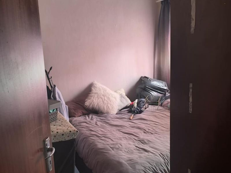 A compact bedroom featuring carpeted flooring and a curtain rail, currently requiring cosmetic updates to the wall finishes and door frame.