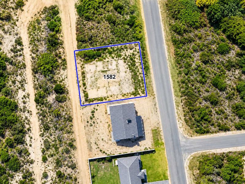 Aerial view of a vacant residential plot featuring a prepared concrete foundation slab, situated in a developed neighborhood with paved road access.