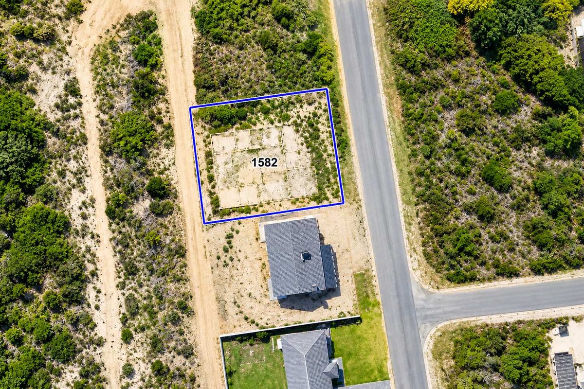Aerial view of a vacant residential plot featuring a prepared concrete foundation slab, situated in a developed neighborhood with paved road access.
