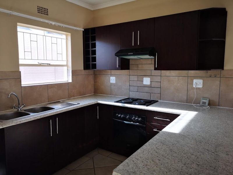 A functional kitchen featuring dark wood cabinetry, granite countertops, a built-in oven with hob, and a double bowl stainless steel sink.