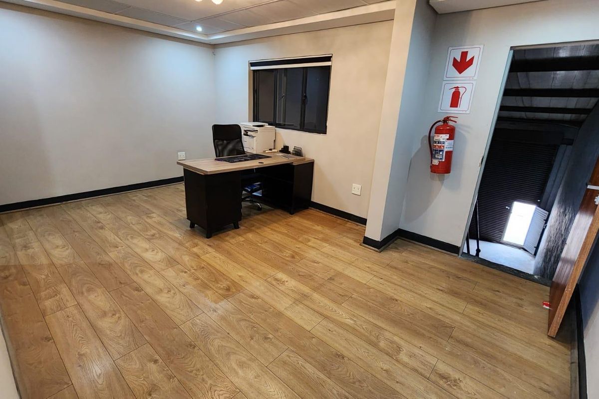 A functional office space featuring wood-look laminate flooring, recessed lighting, and a wall-mounted fire extinguisher, providing a clean and professional work environment.