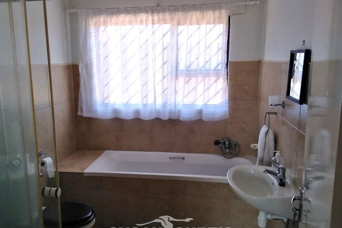 A functional bathroom featuring a built-in bathtub, pedestal sink, toilet, and a separate shower enclosure with tiled walls.
