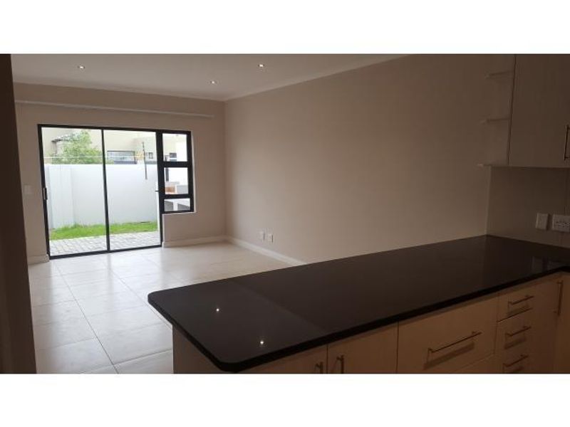 An open-plan living and kitchen area featuring modern cabinetry, dark stone countertops, tiled floors, and a sliding door leading to the rear garden.