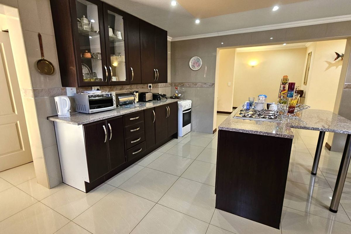 A well-maintained kitchen featuring dark wood cabinetry, granite countertops, a central island with a built-in gas hob, and polished floor tiles.