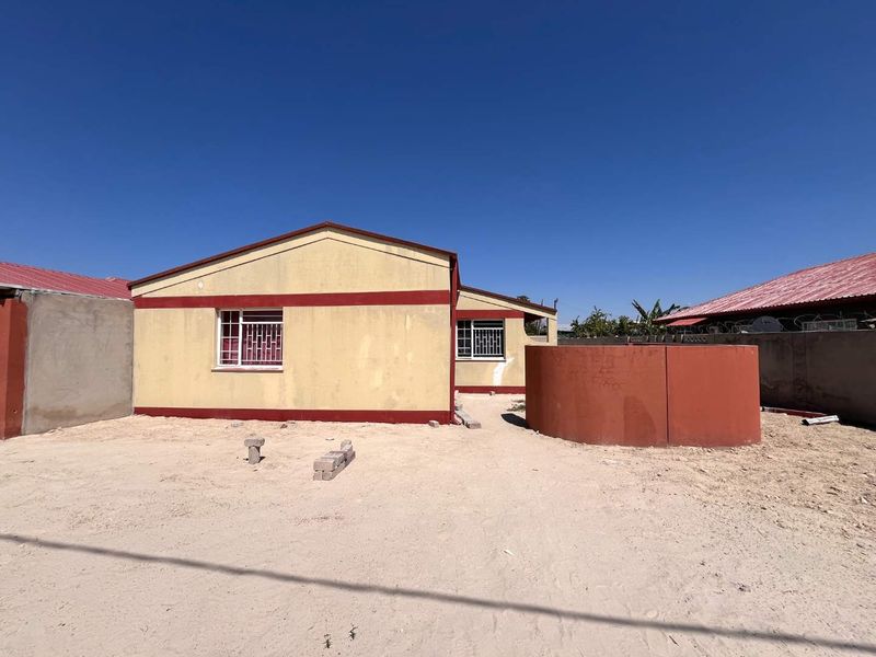 Rear view of the property featuring a painted exterior, metal security bars on windows, a perimeter wall, and a large water tank in the yard.