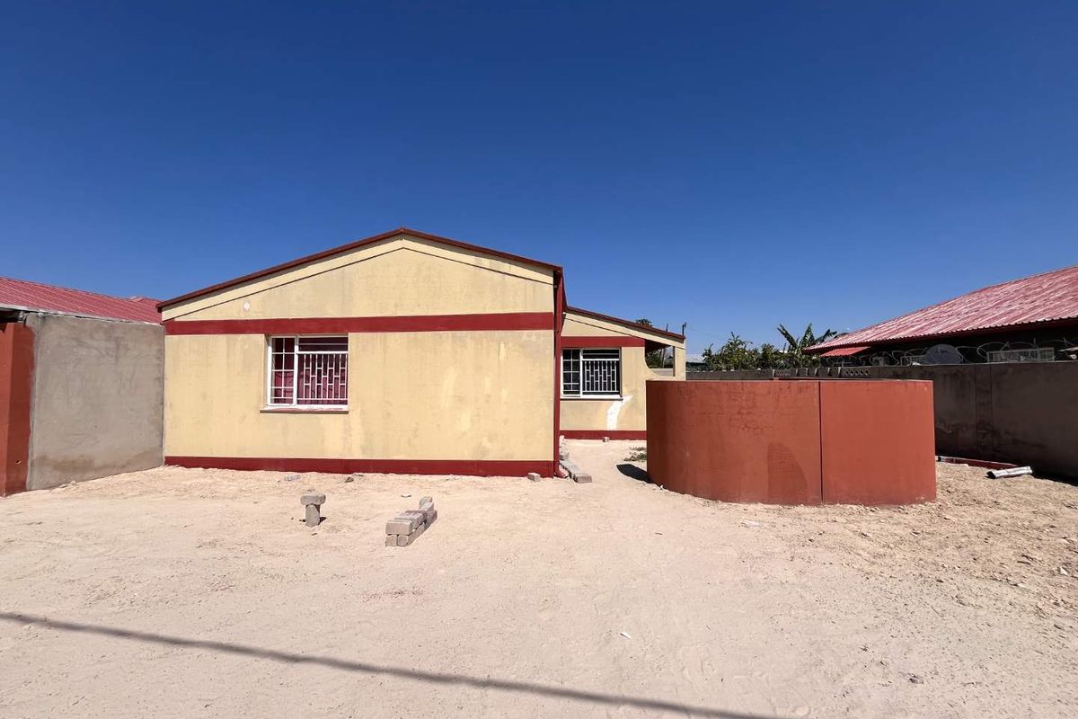 Rear view of the property featuring a painted exterior, metal security bars on windows, a perimeter wall, and a large water tank in the yard.