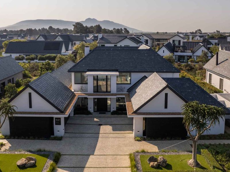 Aerial view of a modern luxury residence featuring a symmetrical facade, double garage, and well-maintained landscaped driveway in a premium estate setting.