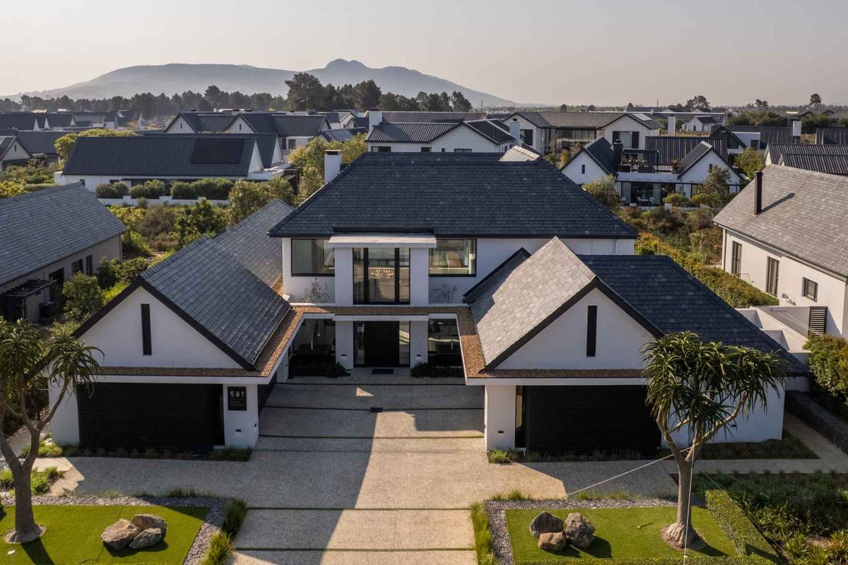 Aerial view of a modern luxury residence featuring a symmetrical facade, double garage, and well-maintained landscaped driveway in a premium estate setting.