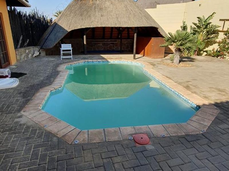 Outdoor pool area featuring a paved patio and a traditional thatched lapa, providing a functional space for outdoor relaxation and entertainment.