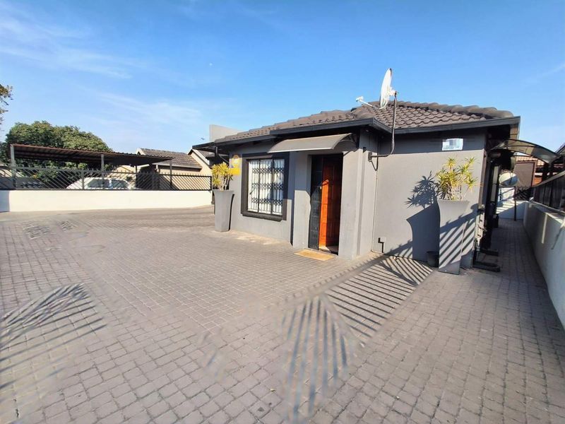 Front view of a single-story house featuring a paved driveway, tiled roof, and secure entrance with a security gate.