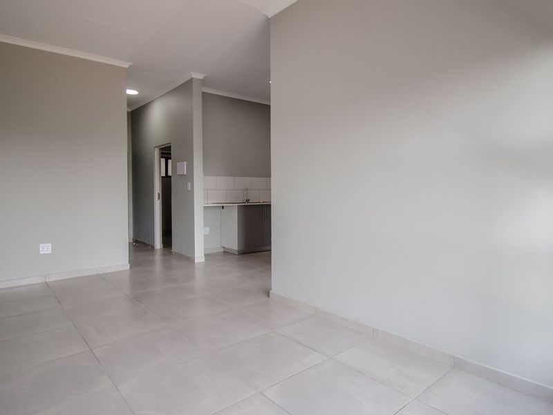 An open-plan living area featuring neutral tiled flooring and a compact kitchen with built-in cabinetry and a sink.