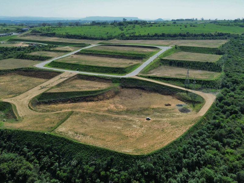 Aerial view of a large industrial development site featuring terraced plots, paved access roads, and surrounding natural landscape.