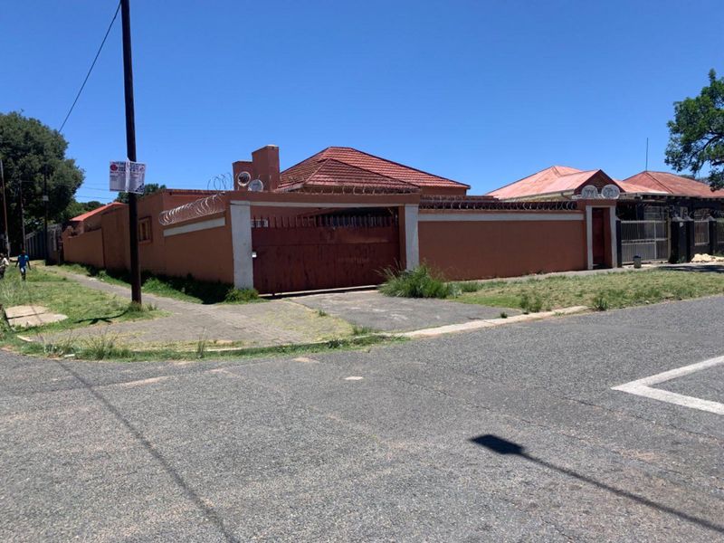 Street view of a residential property featuring a perimeter wall with security razor wire, a metal driveway gate, and a tiled roof structure.