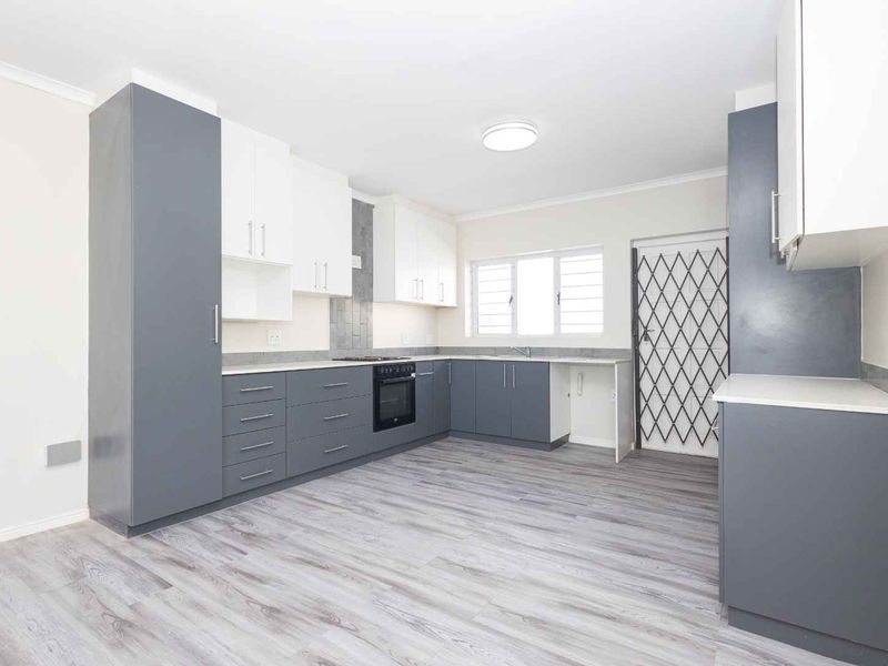 Modern kitchen featuring two-tone cabinetry, built-in oven and hob, laminate countertops, and durable wood-look flooring in a clean, open layout.