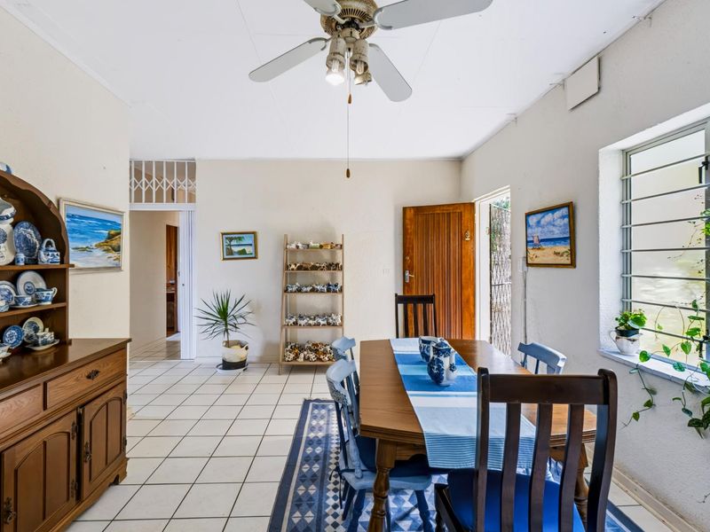 A dining room featuring tiled flooring, a ceiling fan, and natural light through a louvre window, with direct access to an exterior entrance.