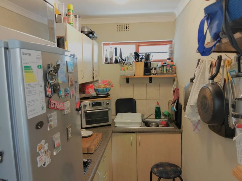 A compact scullery or secondary kitchen area featuring built-in cabinetry, laminate countertops, and a stainless steel sink with tiled splashback.