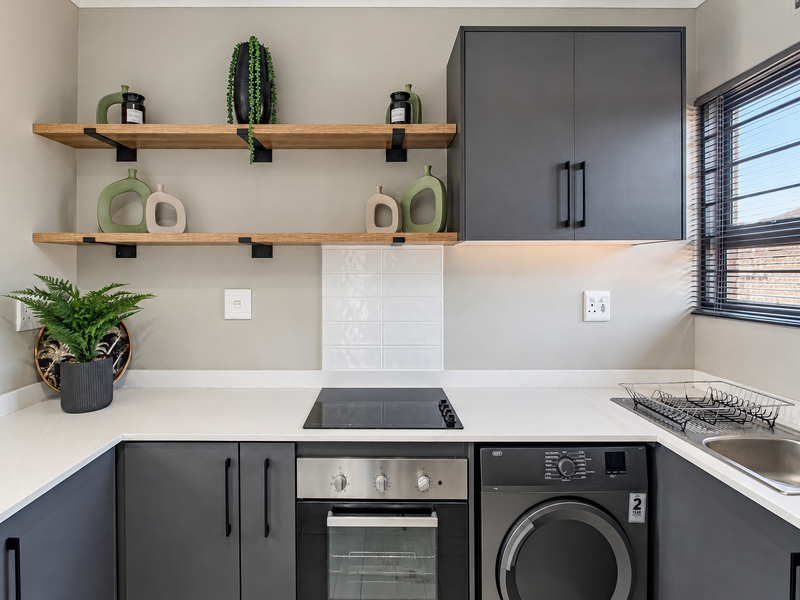 Modern kitchen featuring charcoal cabinetry, quartz countertops, built-in oven, electric hob, and floating timber shelving with a clean subway tile splashback.