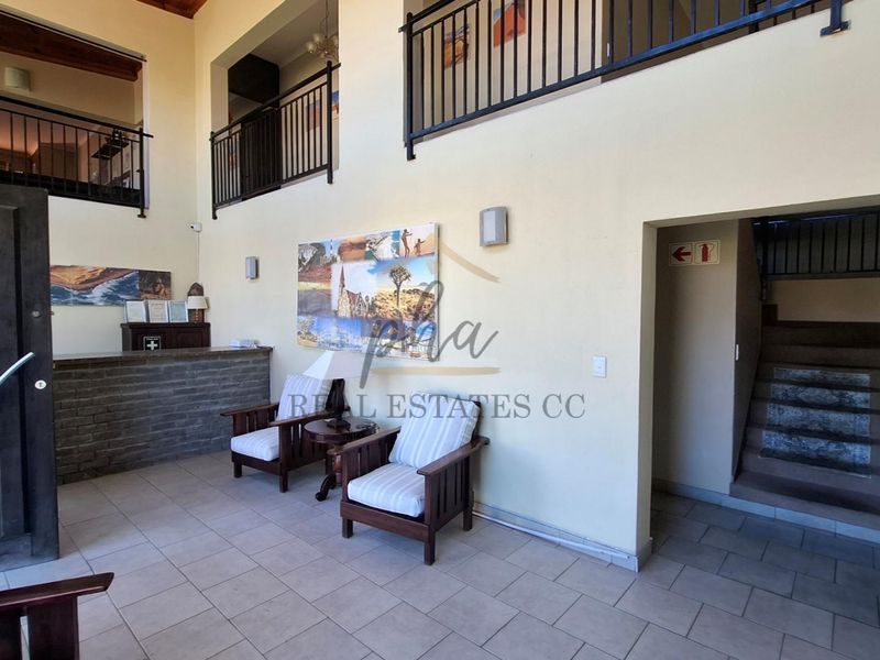Spacious double-volume entrance foyer featuring a reception counter, tiled flooring, and a mezzanine level with metal balustrades overlooking the main area.