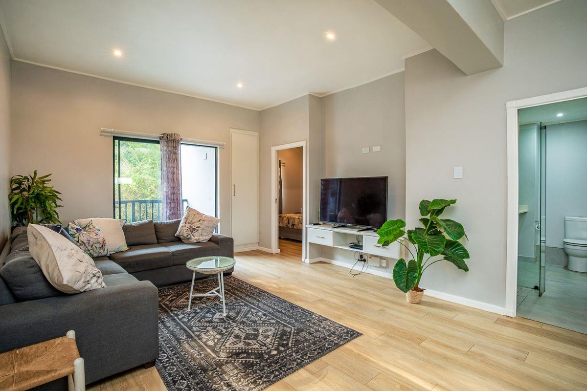 A bright living room featuring light wood-look flooring, recessed ceiling lighting, and direct access to an adjacent bathroom and bedroom.