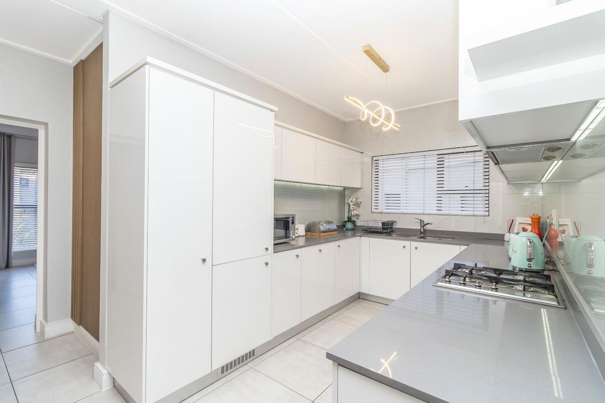 Modern kitchen featuring sleek white cabinetry, stone countertops, a built-in gas hob, and integrated appliances, offering a clean and functional culinary space.