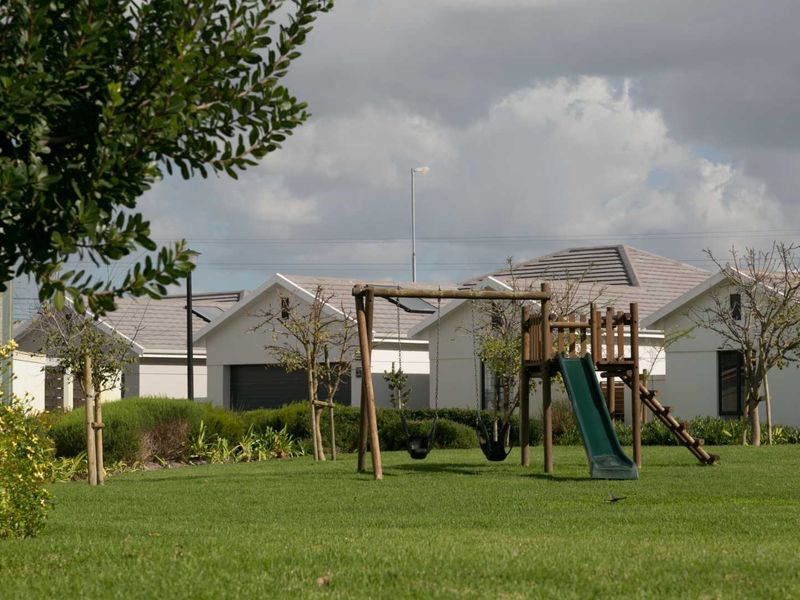 A well-maintained communal garden area featuring a children's playground set, manicured lawn, and surrounding townhouse residential units.