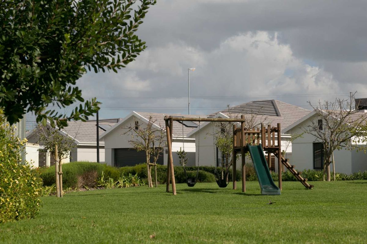 A well-maintained communal garden area featuring a children's playground set, manicured lawn, and surrounding townhouse residential units.