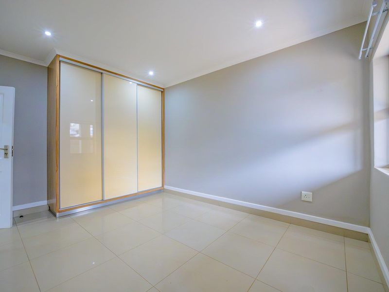 A bright, empty bedroom featuring neutral tiled flooring, recessed downlighting, and a large built-in wardrobe with sliding doors.