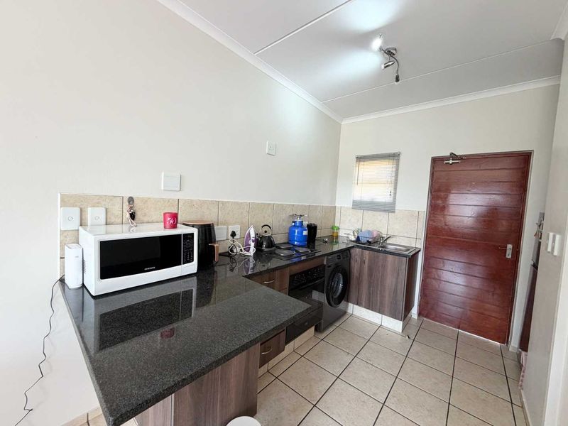 A functional kitchen featuring granite countertops, built-in oven, hob, and tiled finishes, providing a practical workspace with direct access to an exterior door.