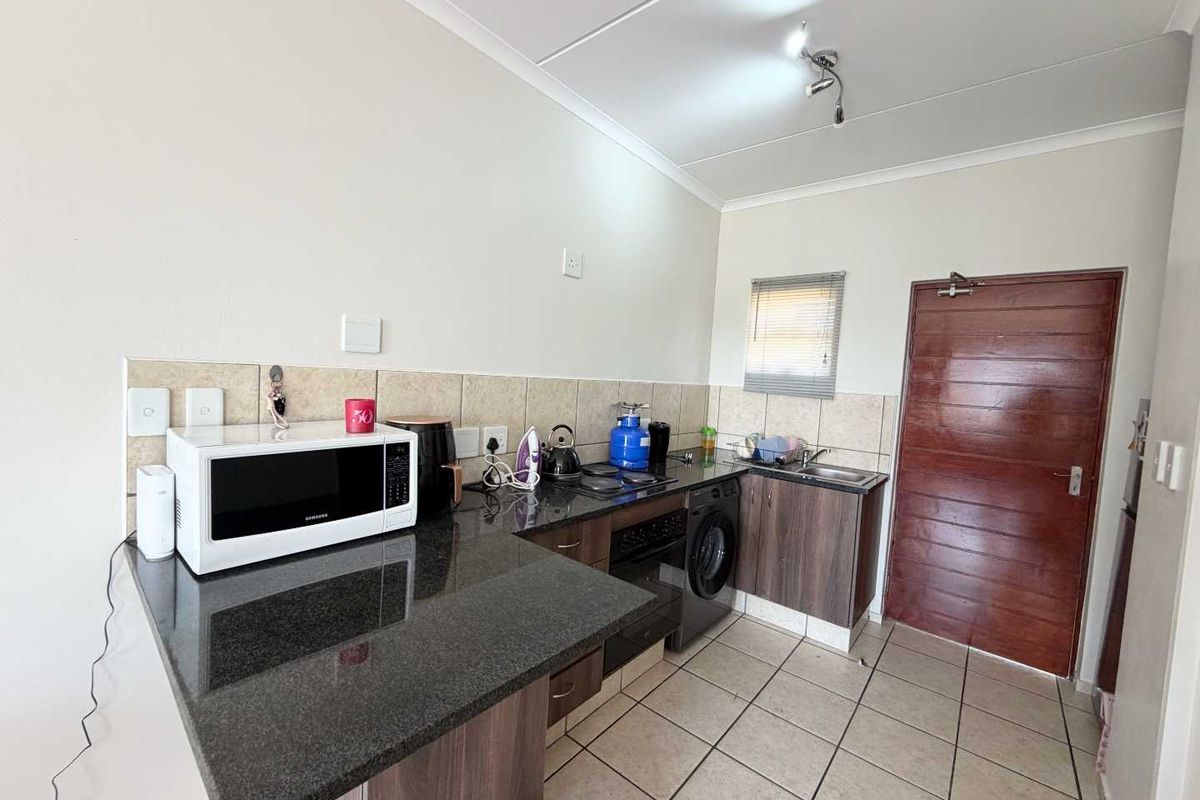 A functional kitchen featuring granite countertops, built-in oven, hob, and tiled finishes, providing a practical workspace with direct access to an exterior door.