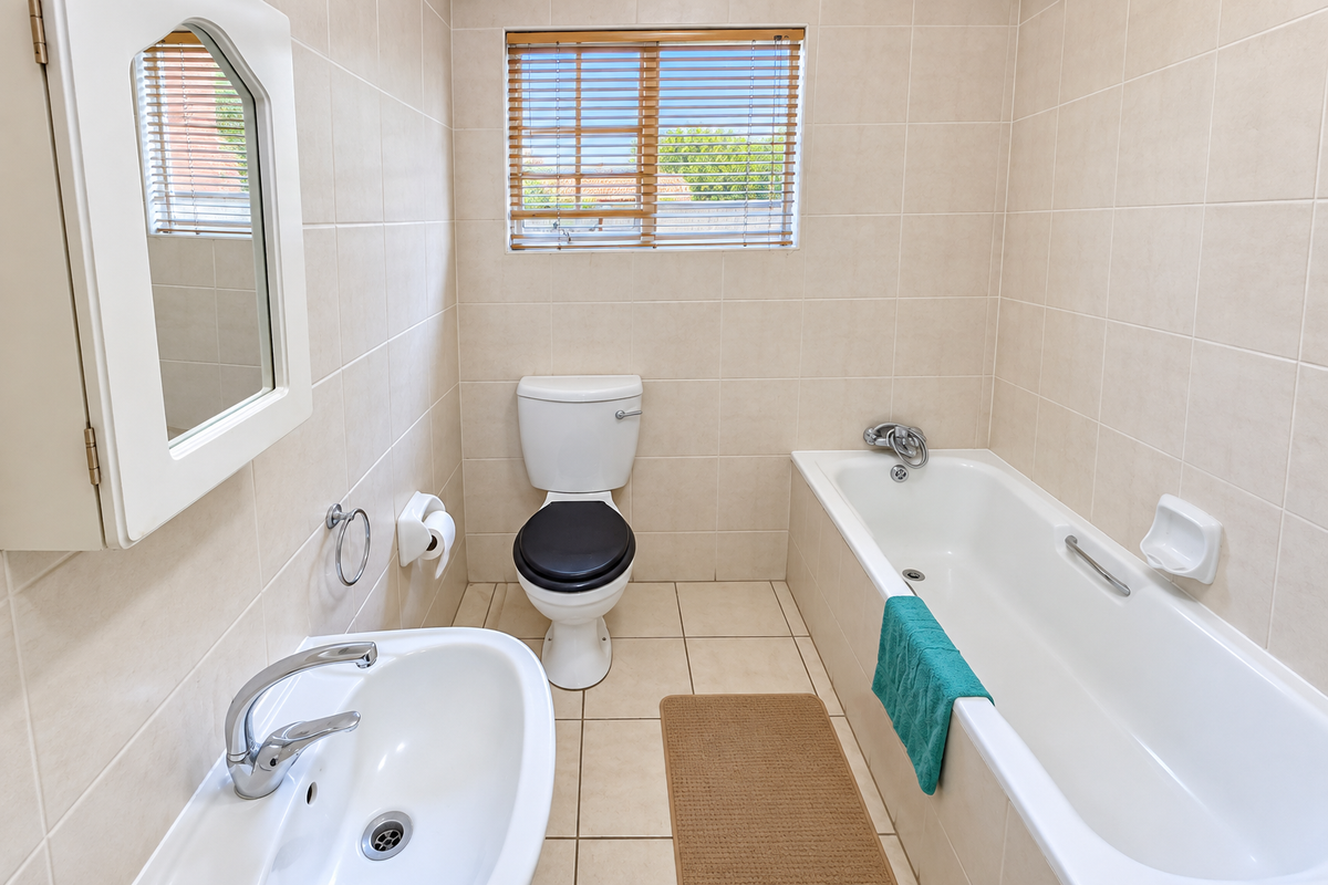 A clean, functional bathroom featuring a bathtub, pedestal basin, and toilet with neutral wall and floor tiling.