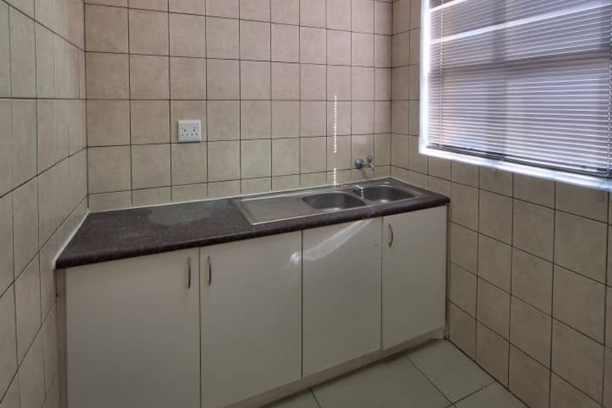 A functional, compact kitchen area featuring white built-in cabinetry, a stainless steel double sink, and full-height wall tiling.