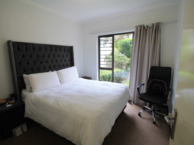 A bedroom featuring carpet flooring, a sliding glass door with security bars, and access to an outdoor garden area.
