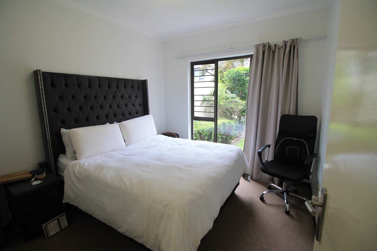 A bedroom featuring carpet flooring, a sliding glass door with security bars, and access to an outdoor garden area.