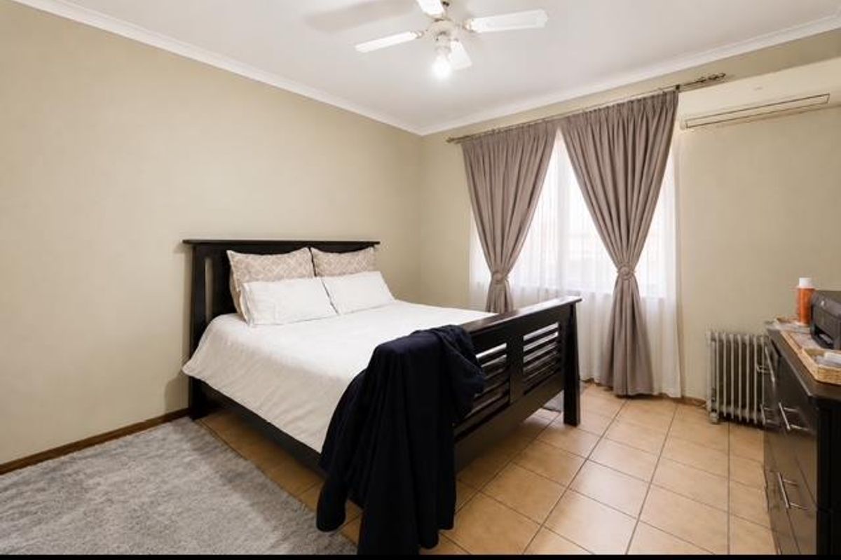 A well-lit bedroom featuring tiled flooring, a ceiling fan, and a wall-mounted air conditioning unit, offering a comfortable and functional living space.