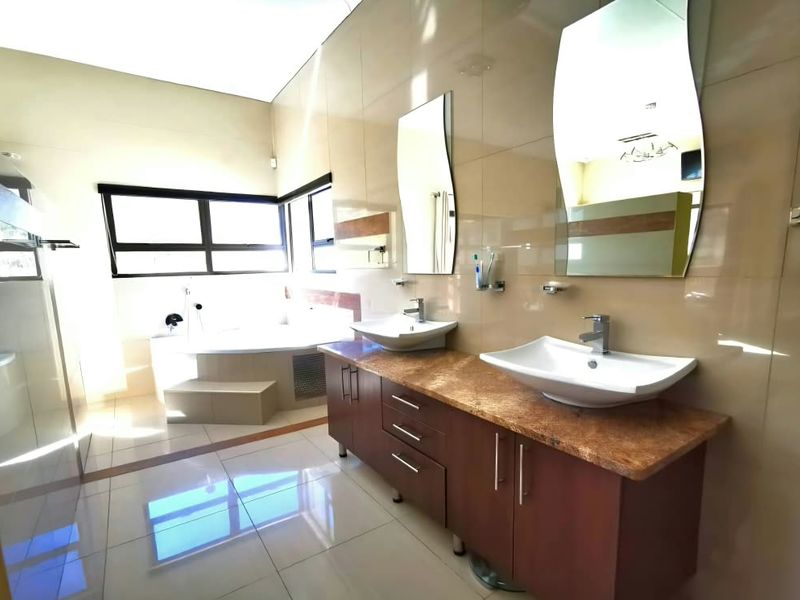 Spacious modern bathroom featuring a double vanity with vessel sinks, tiled finishes, and a built-in bathtub with large windows for natural light.