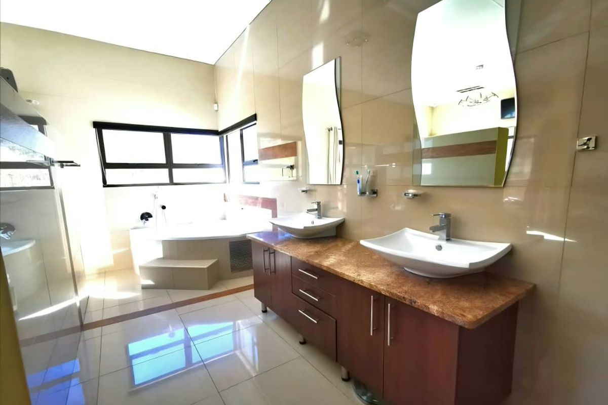 Spacious modern bathroom featuring a double vanity with vessel sinks, tiled finishes, and a built-in bathtub with large windows for natural light.