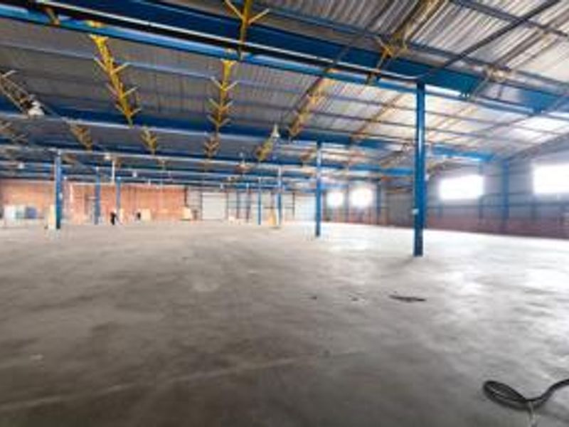 A large, open-plan industrial warehouse space featuring exposed steel structural framing, concrete flooring, and high-clearance corrugated metal roofing.