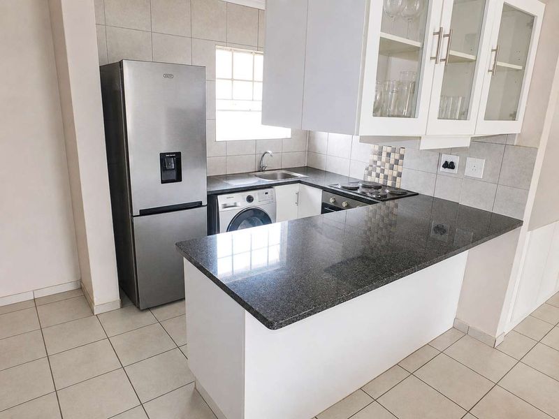 A functional kitchen featuring granite countertops, built-in cabinetry, a hob, oven, and tiled backsplash, providing a clean and practical workspace.
