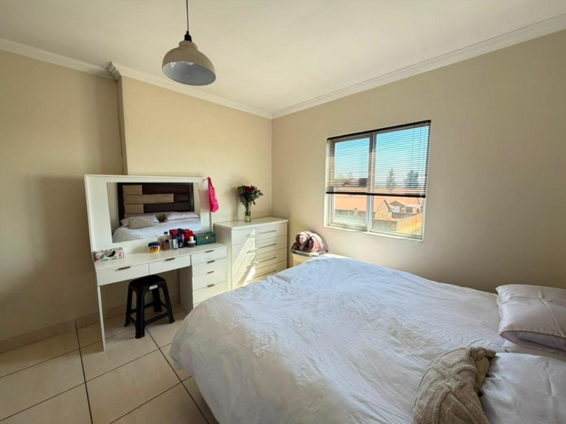 A functional bedroom featuring tiled flooring, neutral wall finishes, and a window with venetian blinds, providing a bright and comfortable living space.