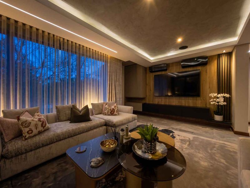 Modern living room featuring a sophisticated media wall with wood paneling, recessed cove lighting, and large windows with elegant sheer curtains.