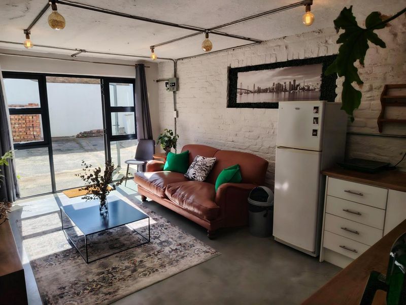 Open-plan living area featuring industrial-style exposed brick walls, polished concrete floors, and large aluminium sliding doors providing access to the exterior.