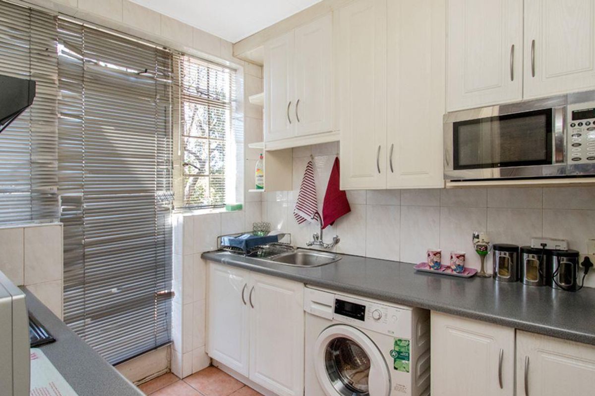 A functional kitchen featuring white cabinetry, a built-in microwave, stainless steel sink, and integrated space for a washing machine.