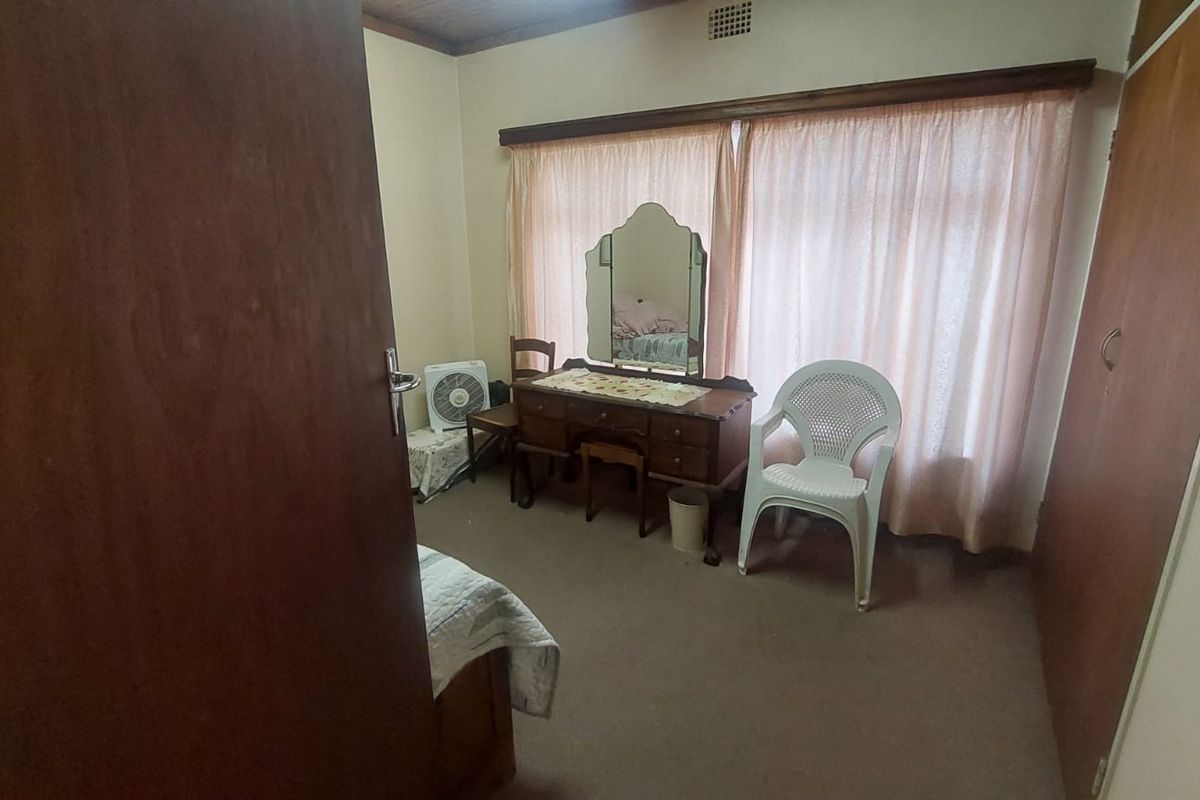 A bedroom featuring built-in wooden cabinetry, carpeted flooring, and a large window with curtains.
