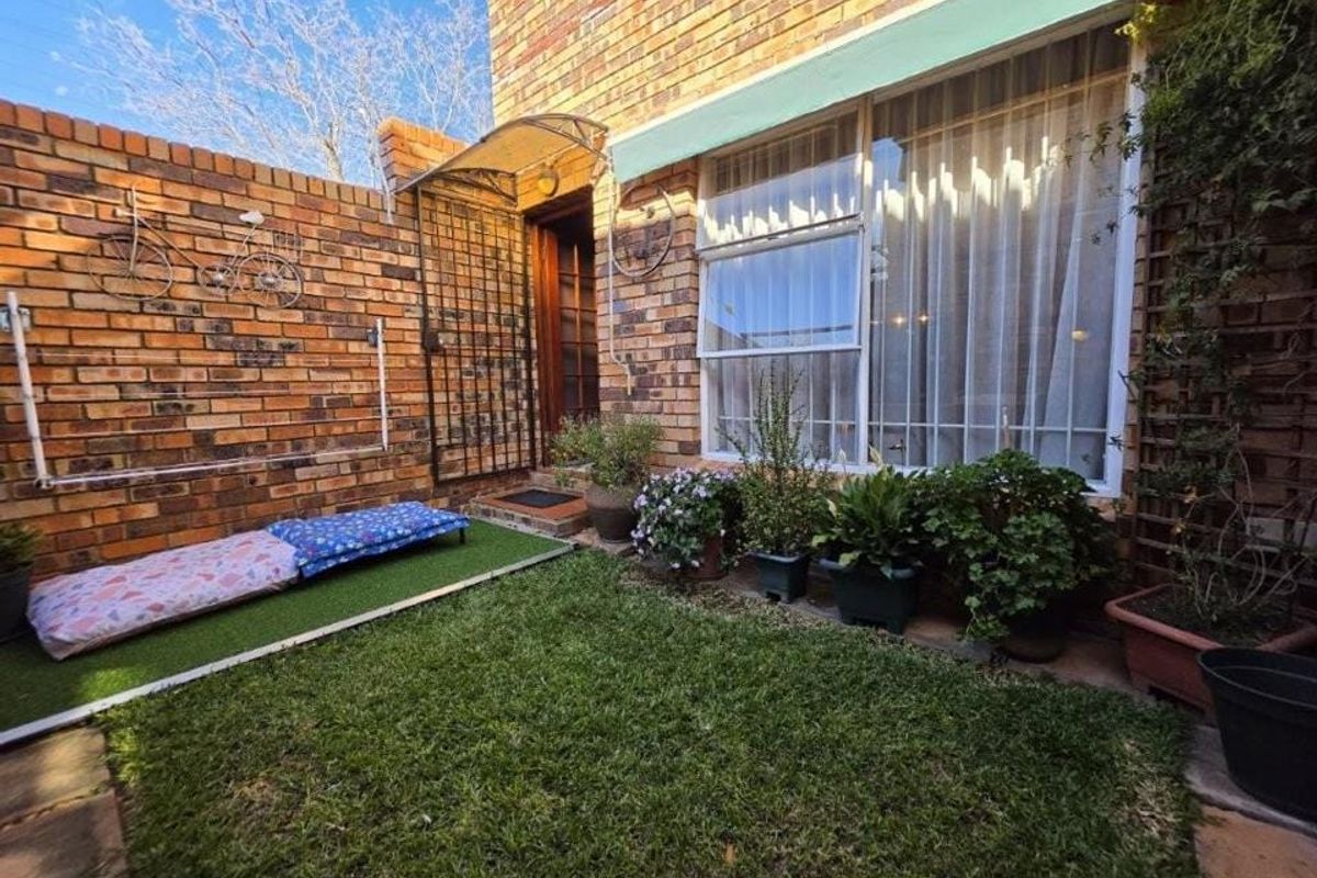 A private rear courtyard featuring face brick walls, a small patch of artificial grass, and a covered entrance area with a security gate.
