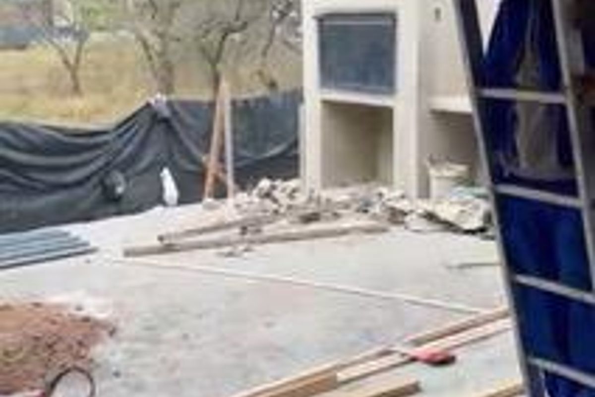 An outdoor patio area currently under construction, featuring a built-in fireplace and exposed structural elements.
